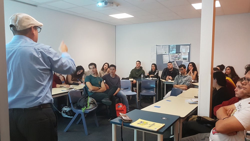 grupo de jóvenes sentados en una clase y un señor explicándoles algo